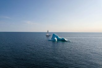 Dogbark sails bye a large iceberg in open water